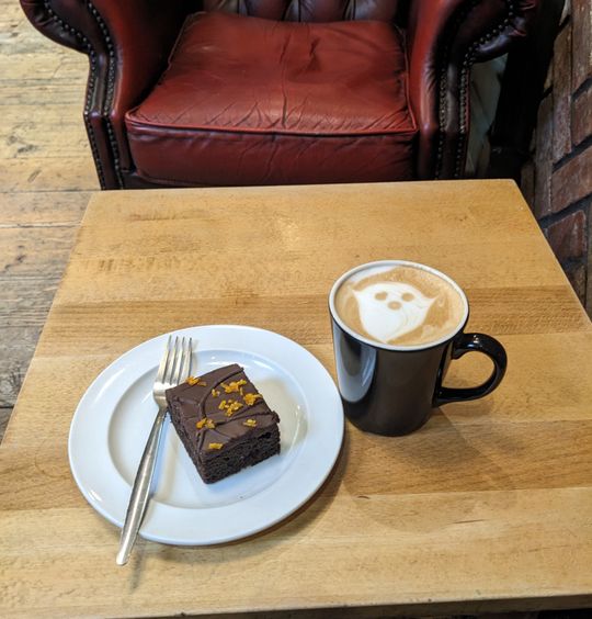 A latte with a ghost latte art. A chocolate orange cake