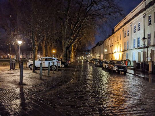 A picture of a wet cobbled road reflecting old street lamps.